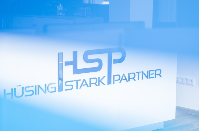 Ein moderner B&uuml;roempfangsbereich. Das Logo H&Uuml;SING STARK PARTNER und die Initialen HSP sind zu sehen.