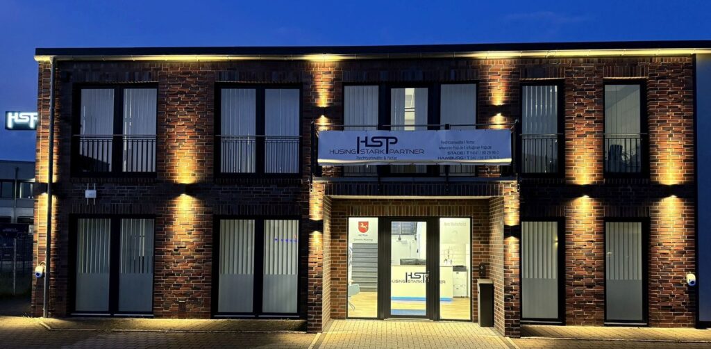 Ein modernes Backsteingebäude mit Beleuchtung und einem großen Schild mit der Aufschrift „Hüsing Stark Partner Rechtsanwälte & Notar“.