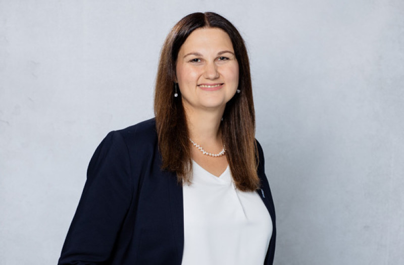 Frau Sonja Schumacher mit glattem braunem Haar, trägt einen marineblauen Blazer, eine weiße Bluse und einer Perlenkette. Lächelt in die Kamera.