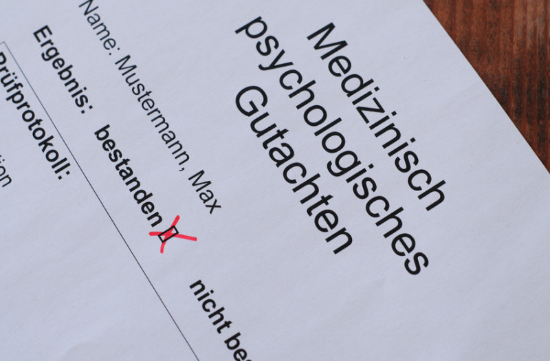 Nahaufnahme eines deutschen medizinisch-psychologischen Gutachtens. „Bestanden“ ist mit einem roten Häkchen neben dem Namen Max Mustermann markiert.