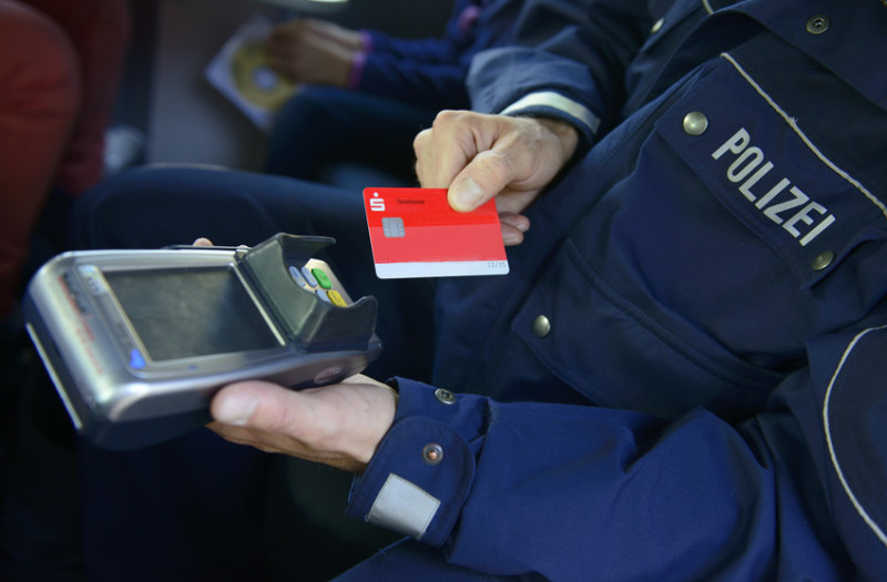 Eine Person in einer Polizeiuniform mit der Aufschrift „POLIZEI“ hält ein Zahlungsterminal, während eine andere Hand eine rote Sparkassekarte vorlegt.
