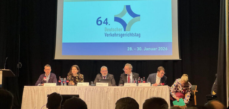 Sechs Personen sitzen auf dem Podium an einem Tisch. Im Hintergrund sind auf der Leinwand das Logo und der Schriftzug des 64. Deutschen Verkehrsgerichtstages zu sehen.