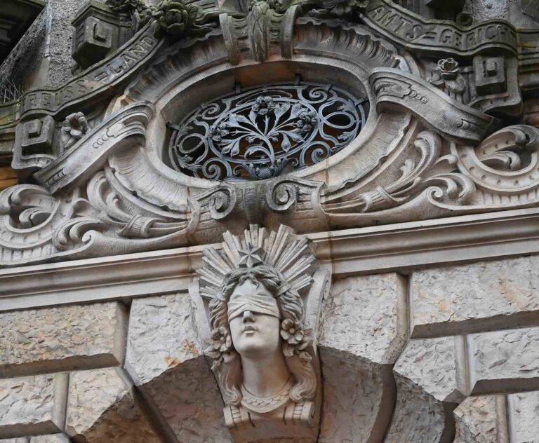 Portal eines alten Gebäudes mit dem steinernen Schriftzug "Amtsgericht" und einer steinernen Justitia mit verbundenen Augen